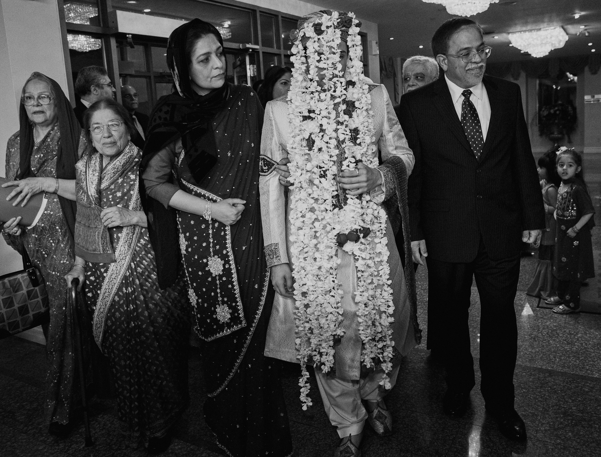 Indian groom in flower veil being led to ceremony by family