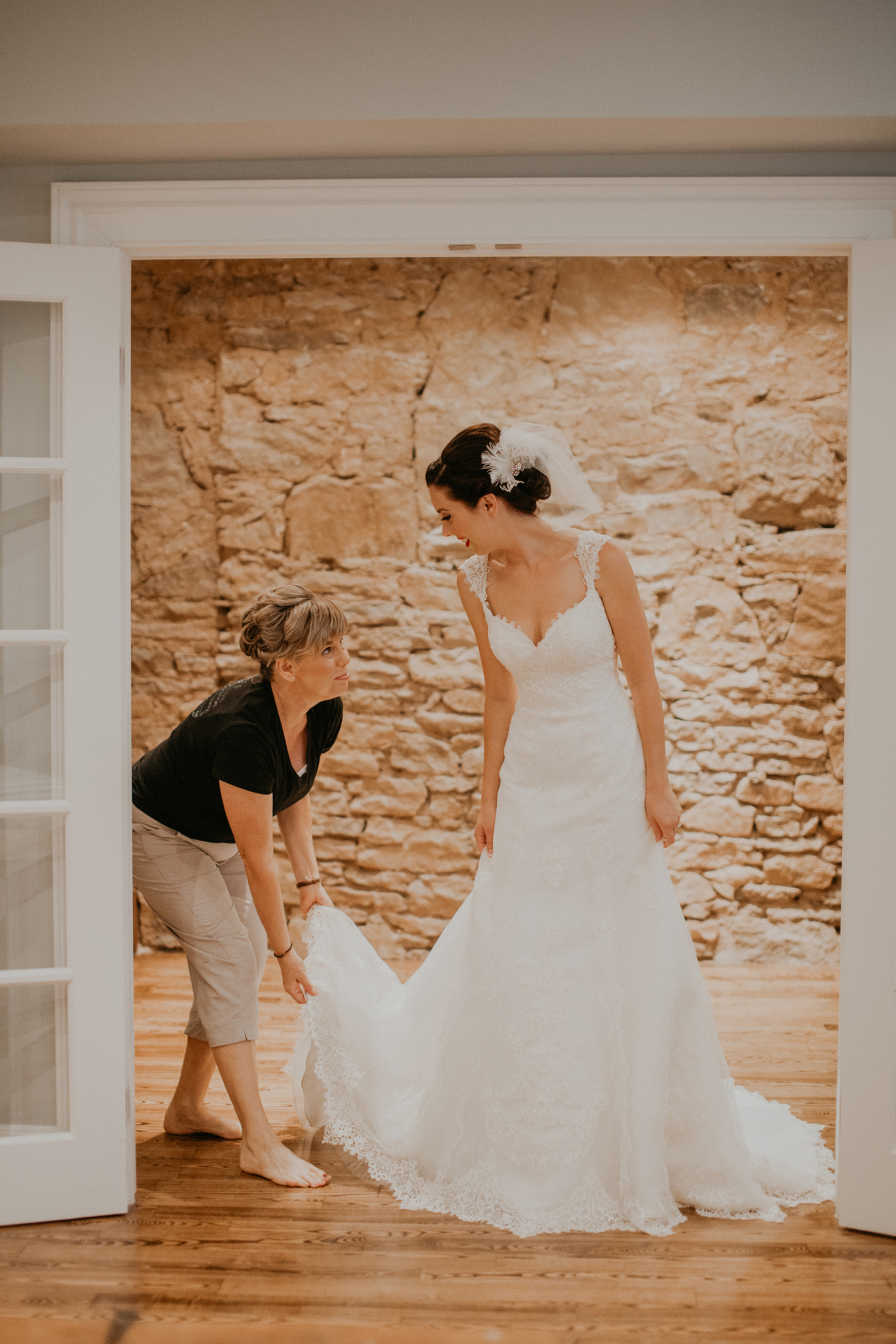 Mother of bride helps bride put on wedding dress