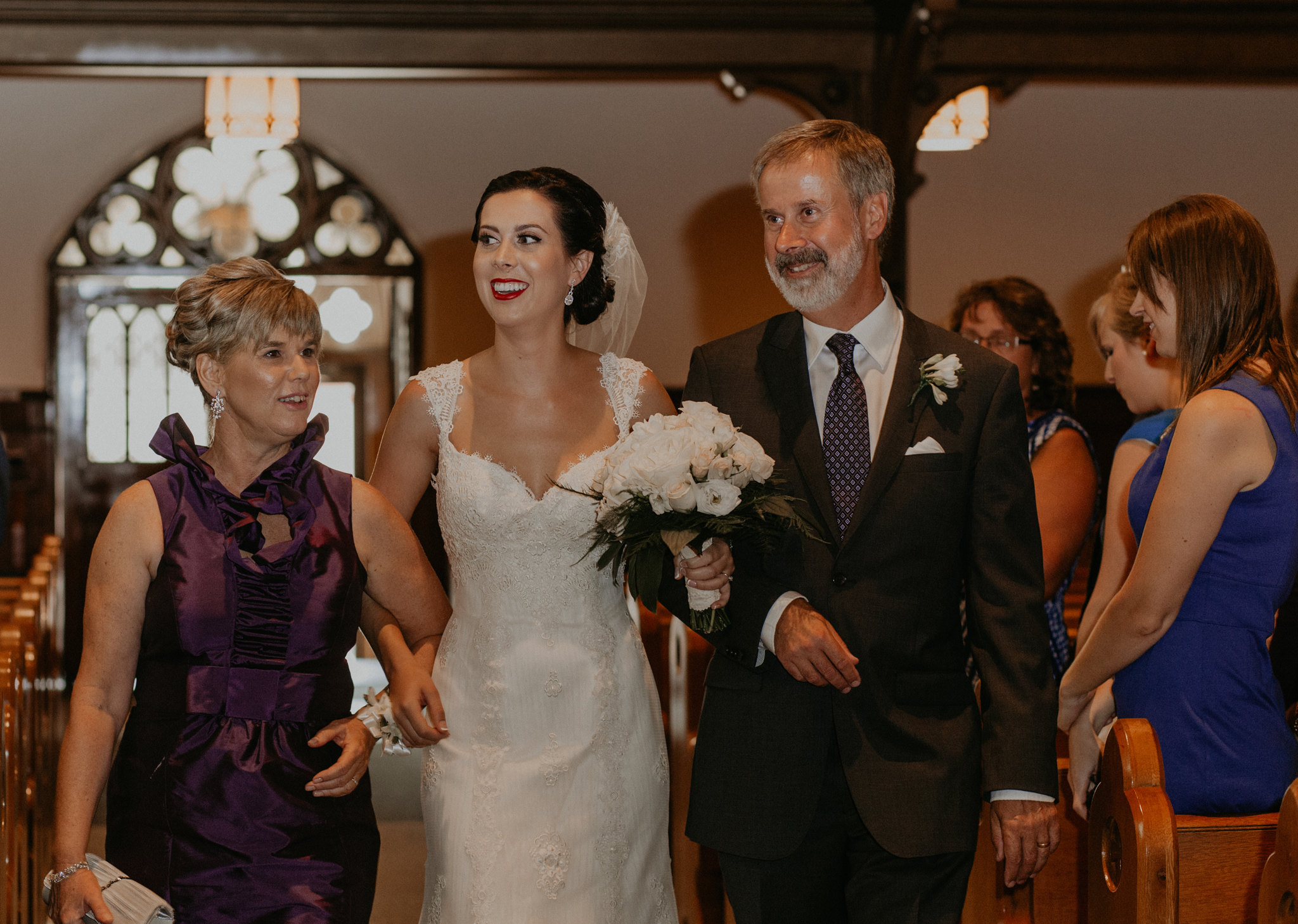 Bride walks up aisle with mom and dad during church ceremony