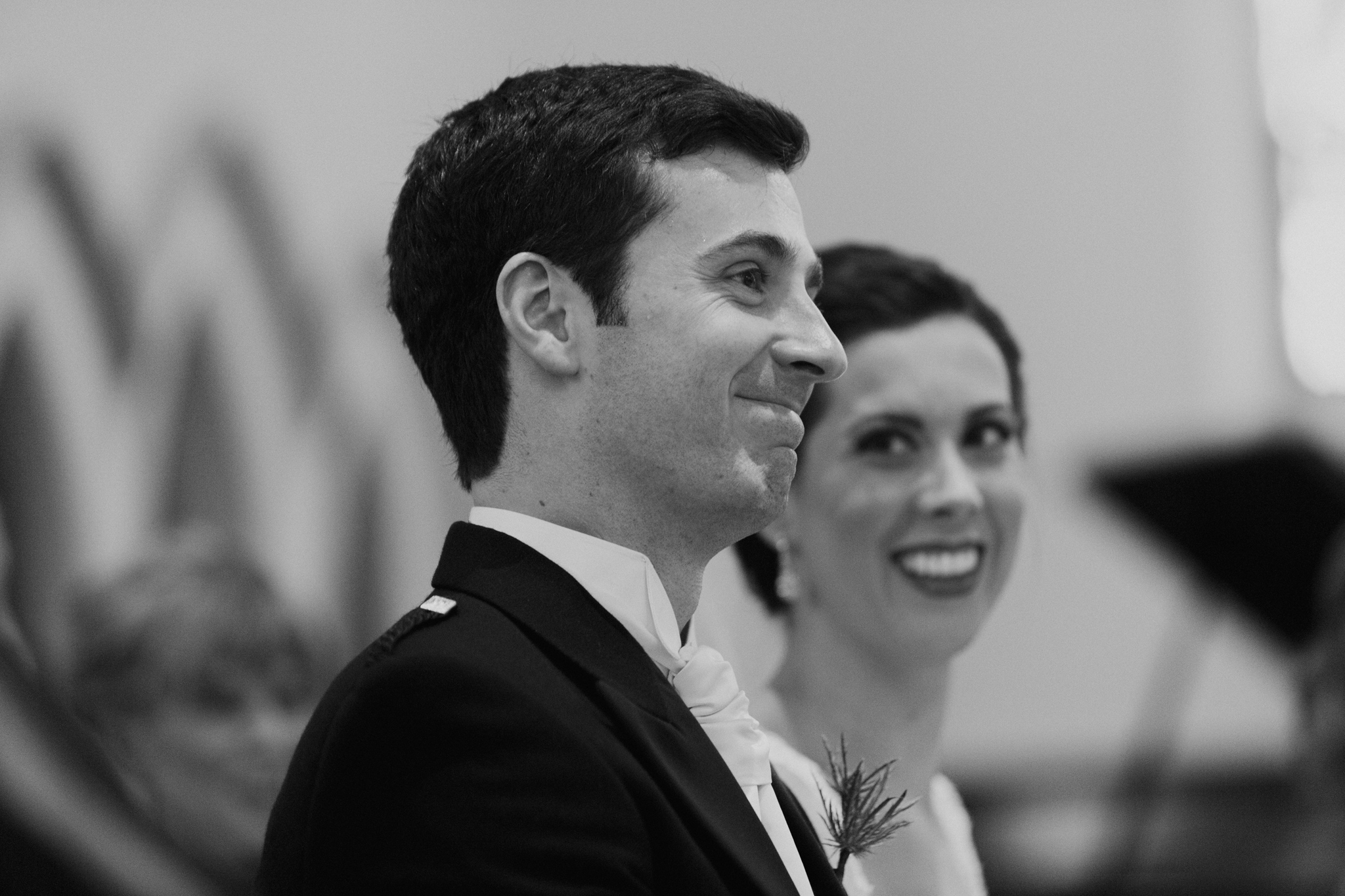 Bride smiles at groom while groom smiles and looks forward in church ceremony