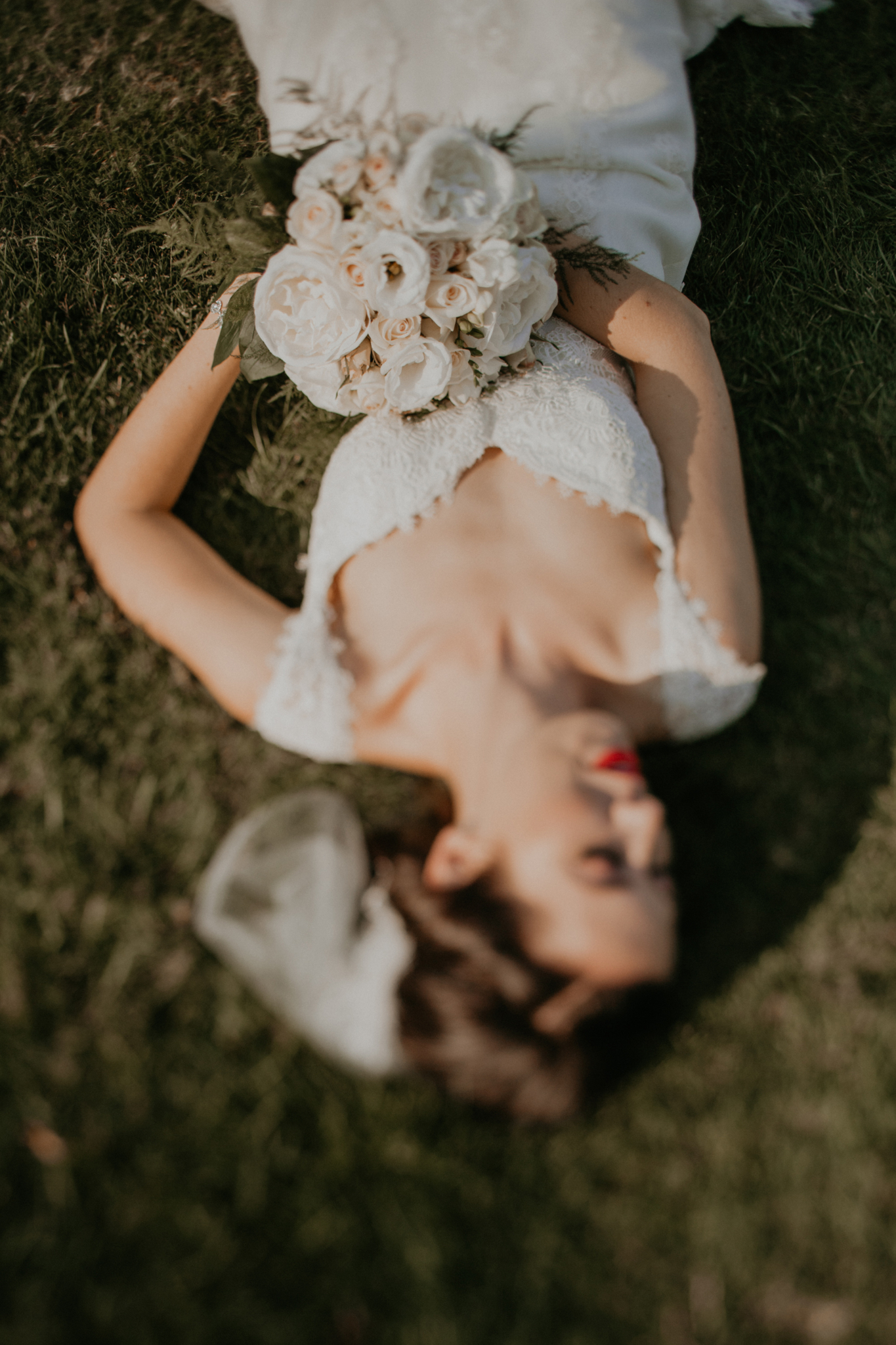 Bride lays down in grass holding bouquet