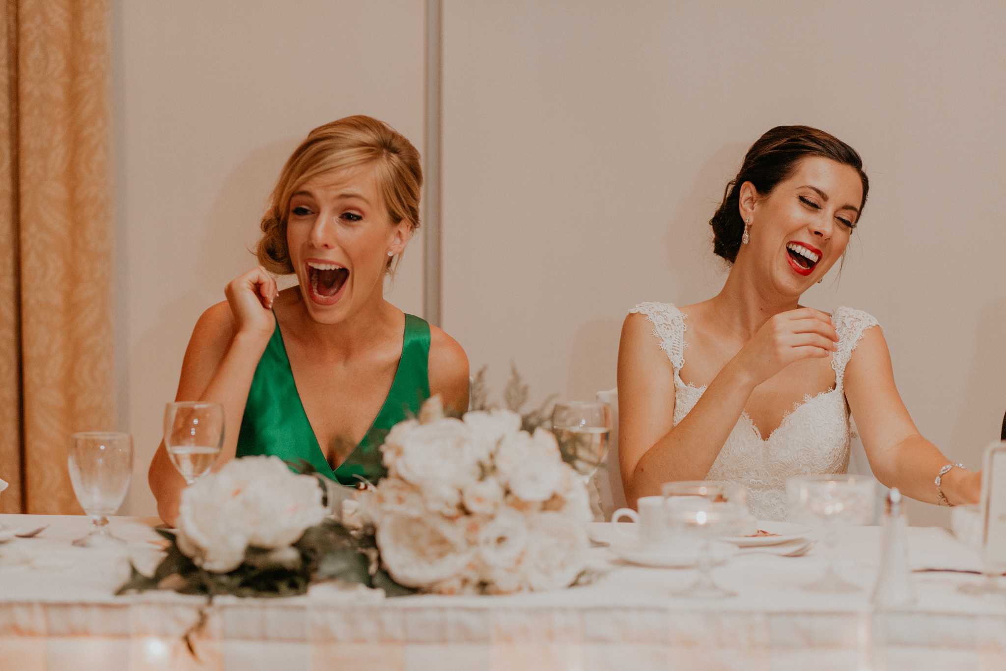 Candid of bride and bridesmaid laughing during wedding reception speeches