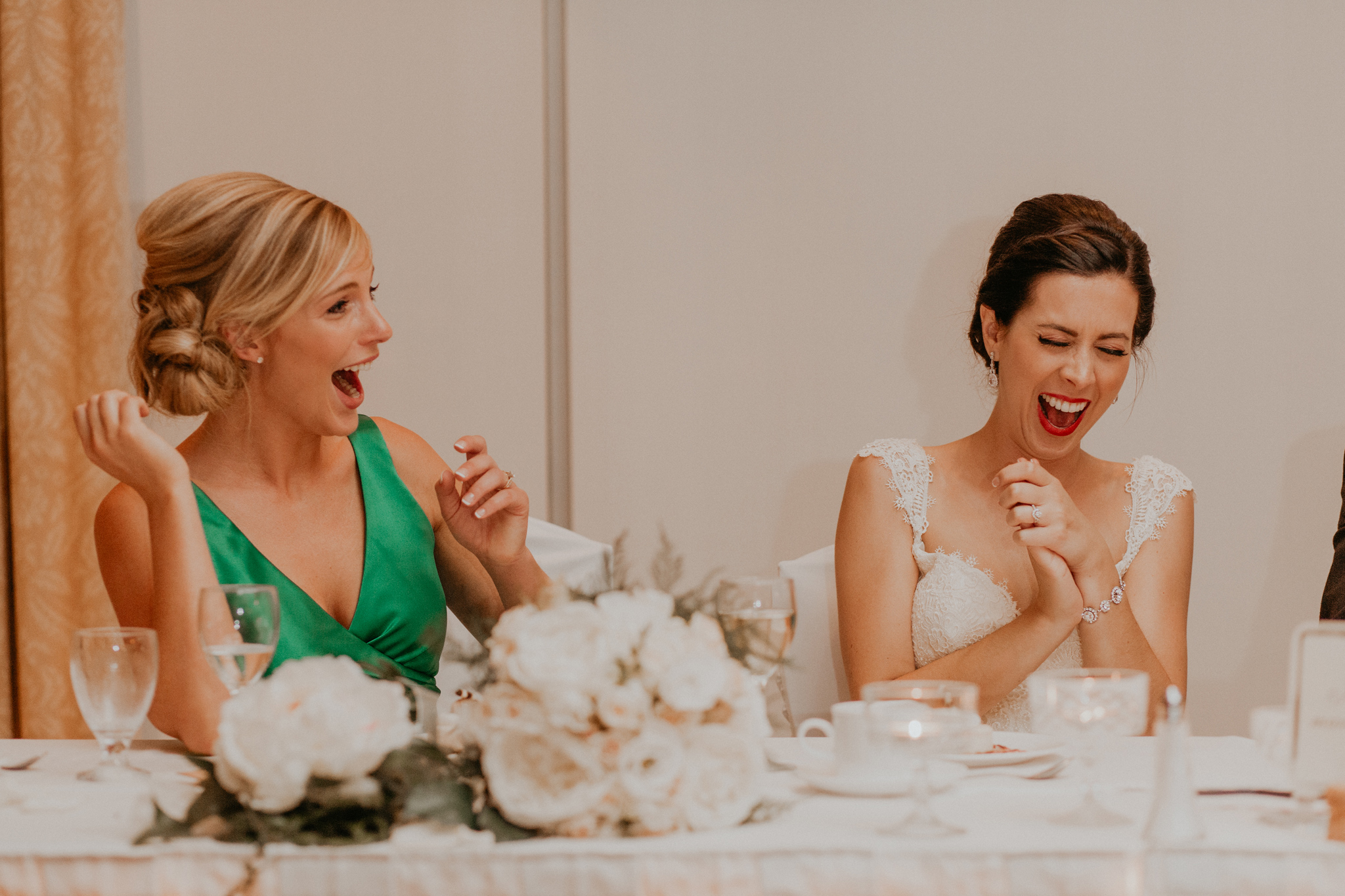 Bride and bridesmaid laugh during wedding reception speeches