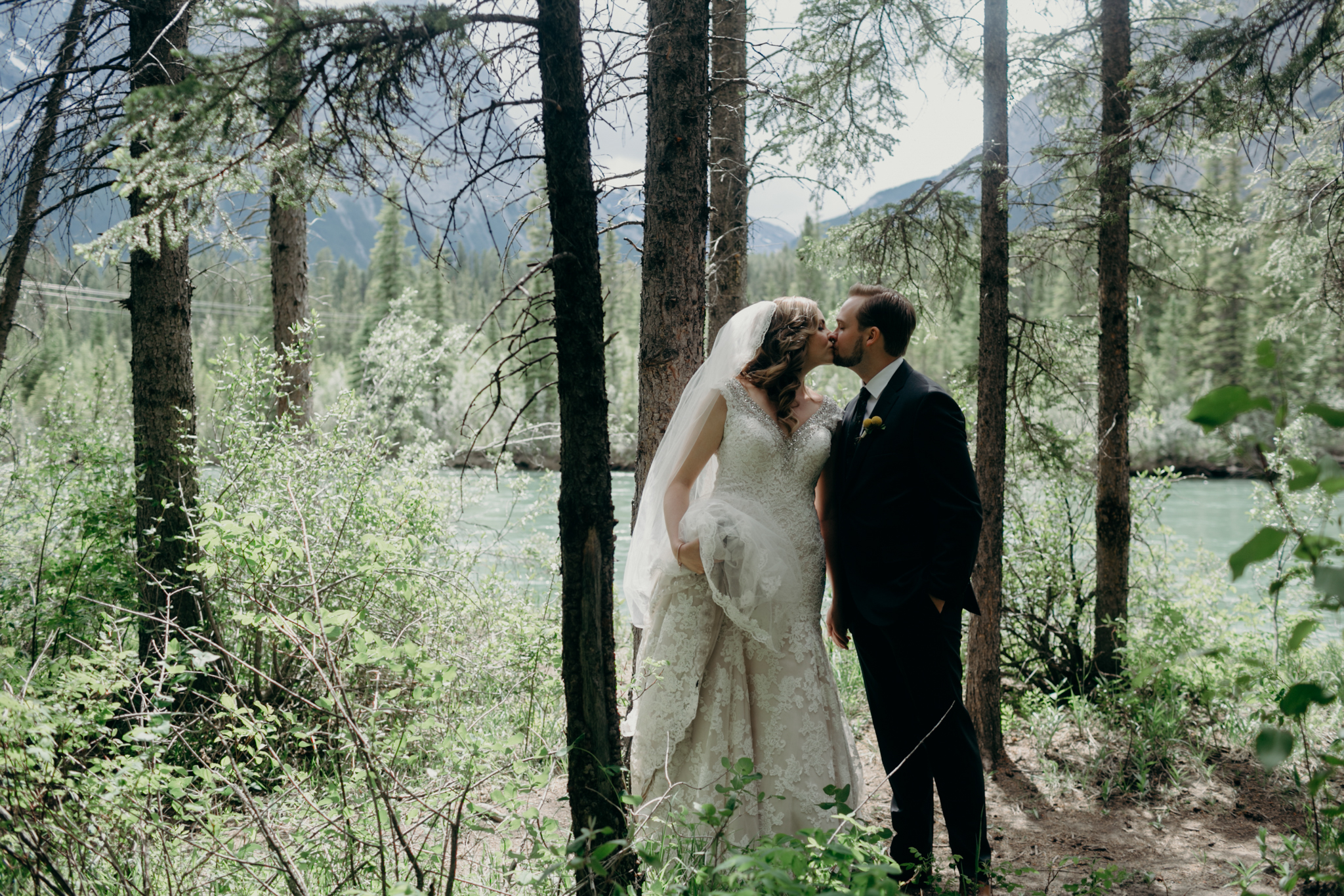 Bride and groom kiss with mountains and Bow River in background romantic Canmore photo