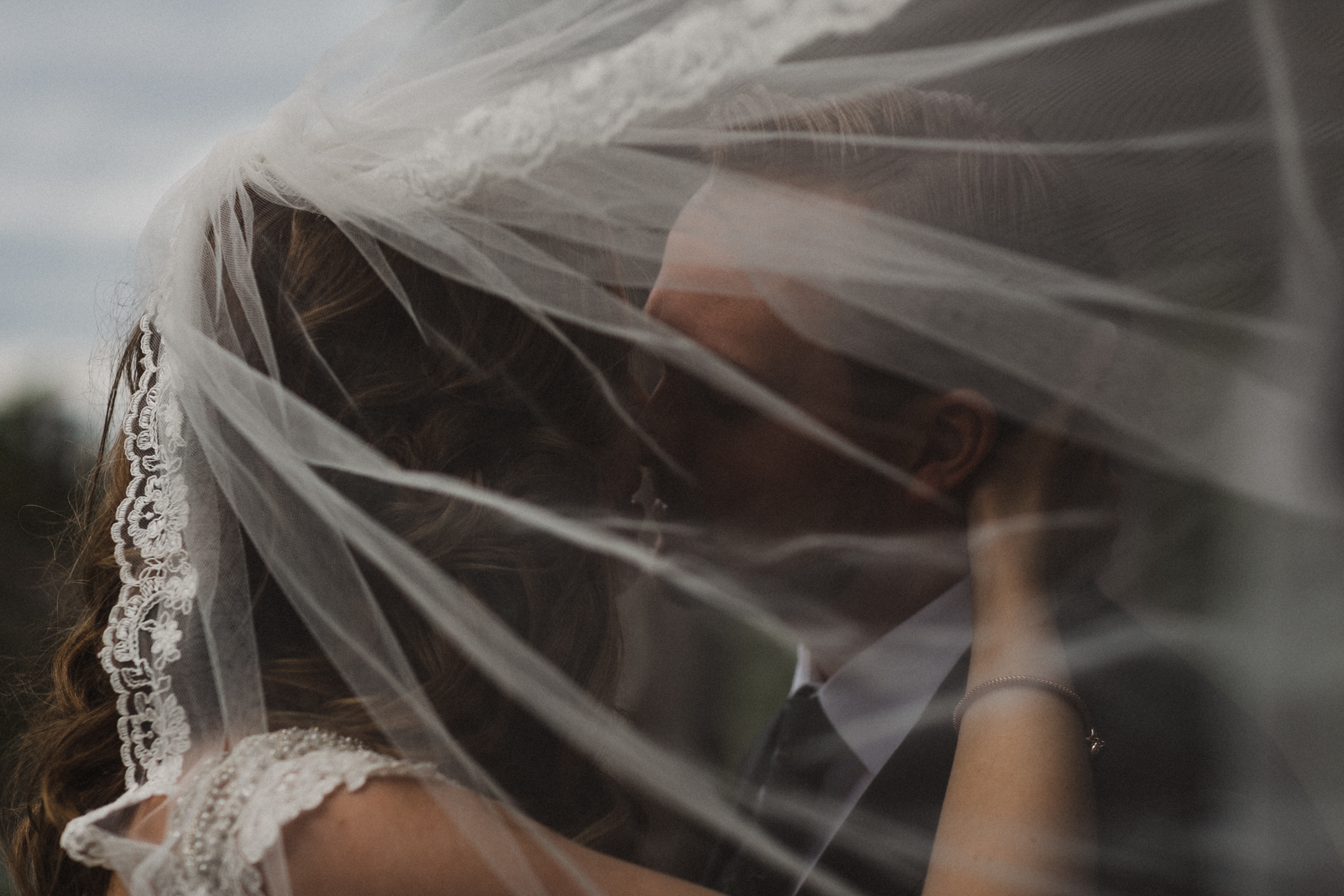 Bride and groom embrace underneath veil in moody portrait