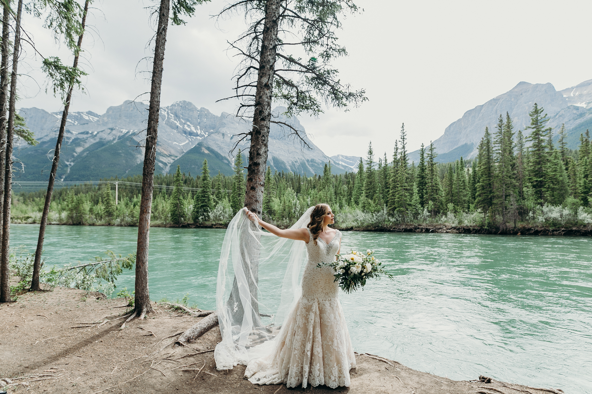 Bride plays with veil on edge of Bow River Canmore AB