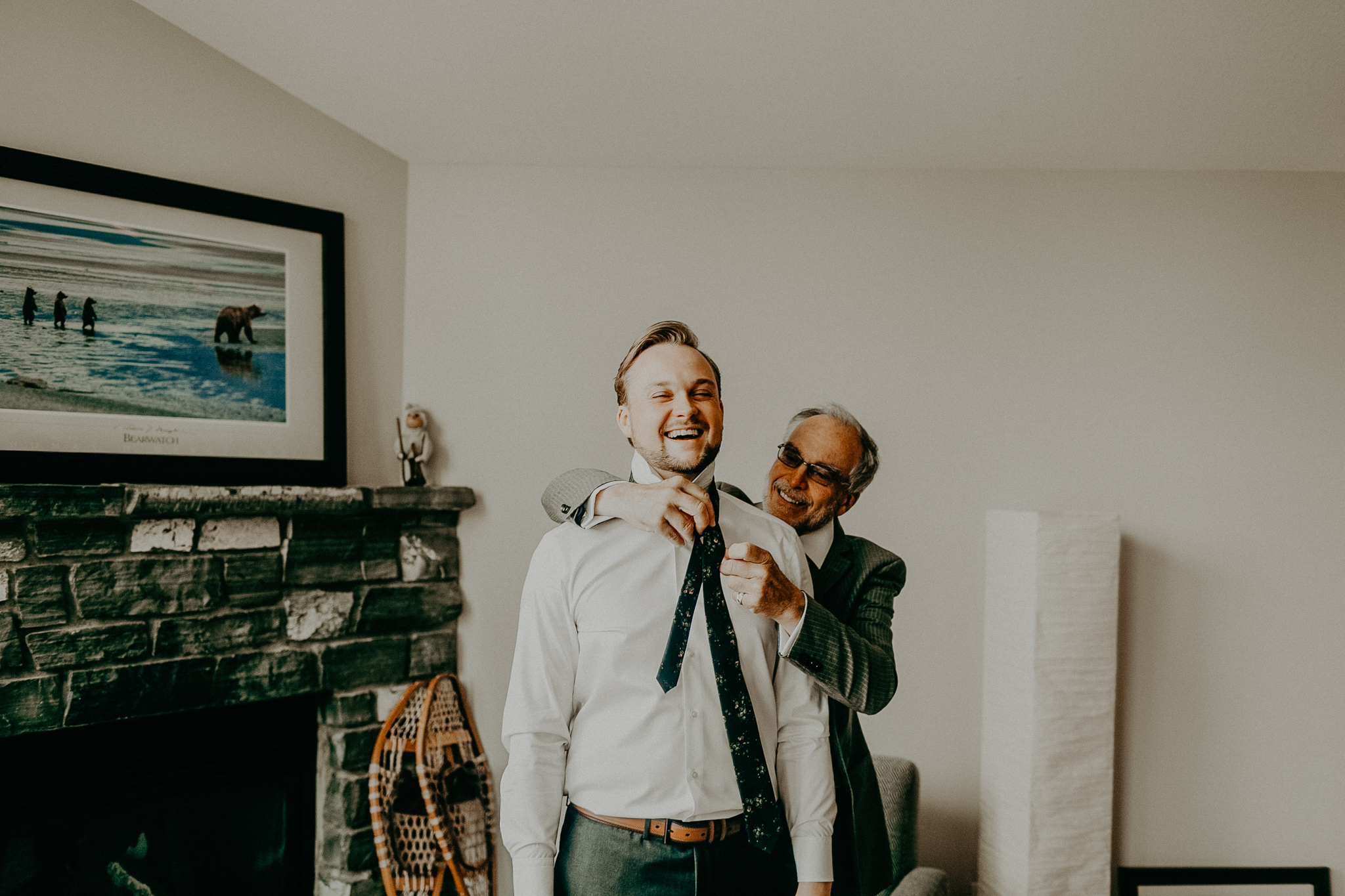 Groom's dad helps groom tie on tie in hotel room while getting ready for wedding
