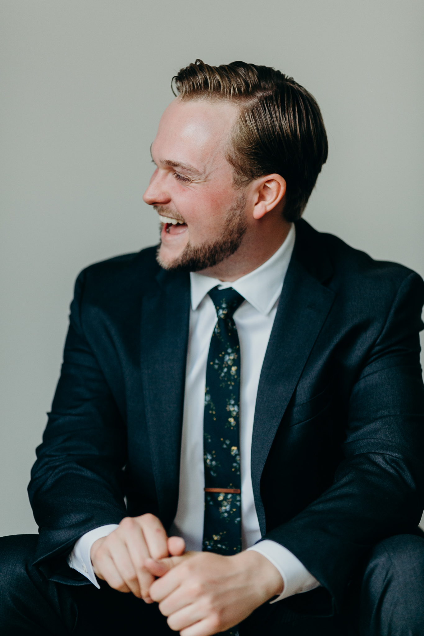 Candid portrait of groom in suit against white wall laughing