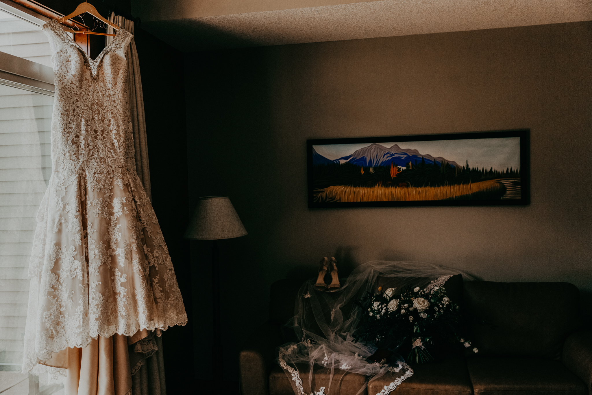 Bride's wedding dress hanging from doorframe with veil and flowers