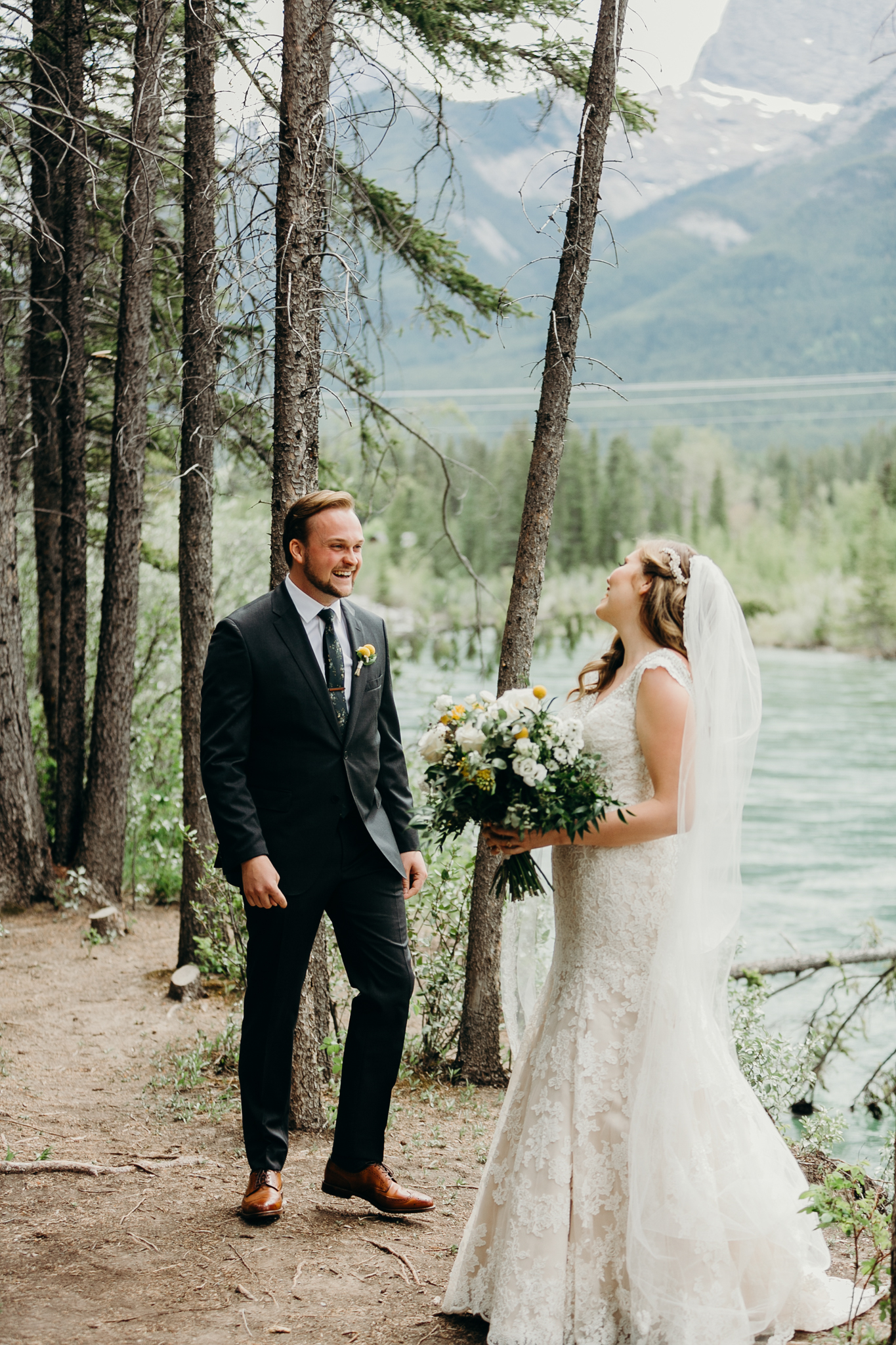 Groom sees bride during first look smiling with Bow River and mountains in background Canmore AB