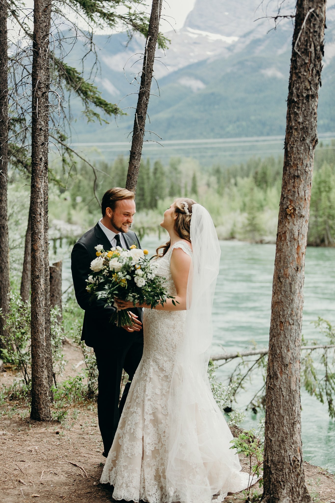 Groom sees bride during first look smiling with Bow River and mountains in background Canmore AB