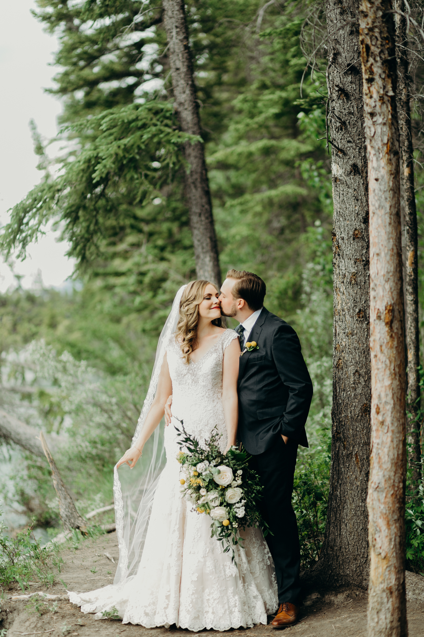 Bride and groom kiss in front of evergreens wedding portrait in Canmore AB